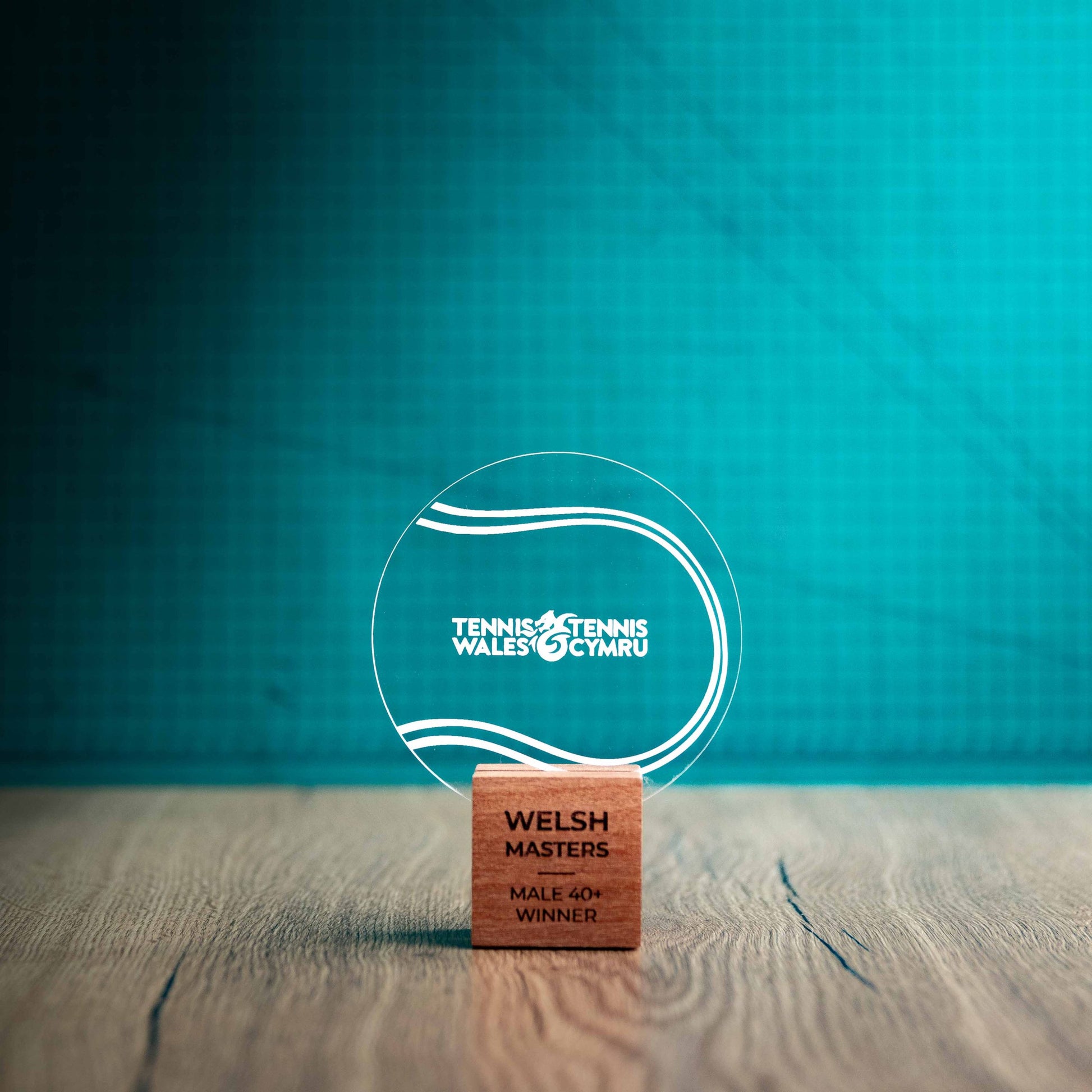 A small Tennis trophy with custom text and logos, on an eco-friendly wooden base, with a clear Perspex Tennis ballmounted on top, featuring fully customisable areas for text and logos.