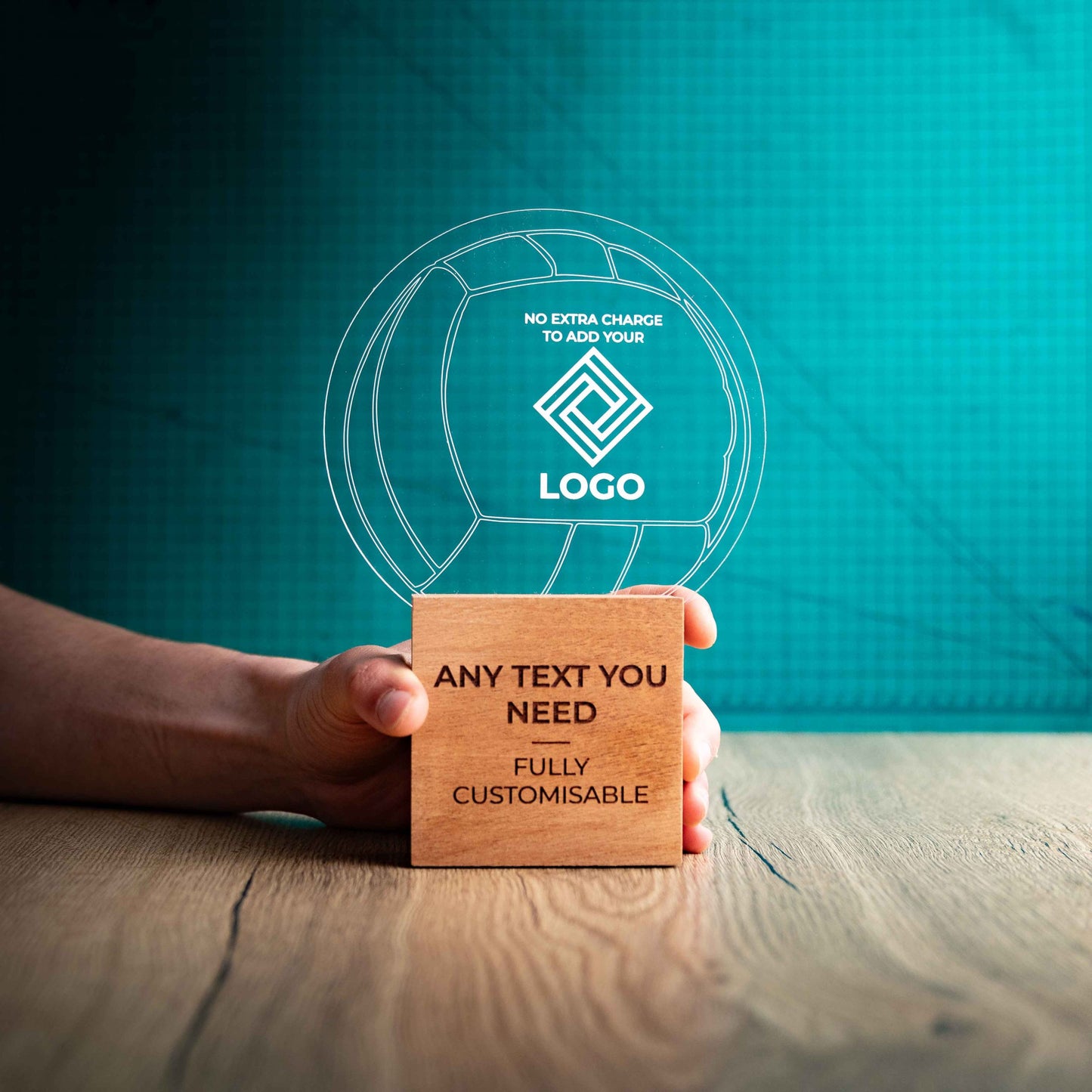 A large Volleyball trophy with custom text and logos, on an eco-friendly wooden base, with a clear Perspex Volleyball mounted on top, featuring fully customisable areas for text and logos, being held to give a size perspective.