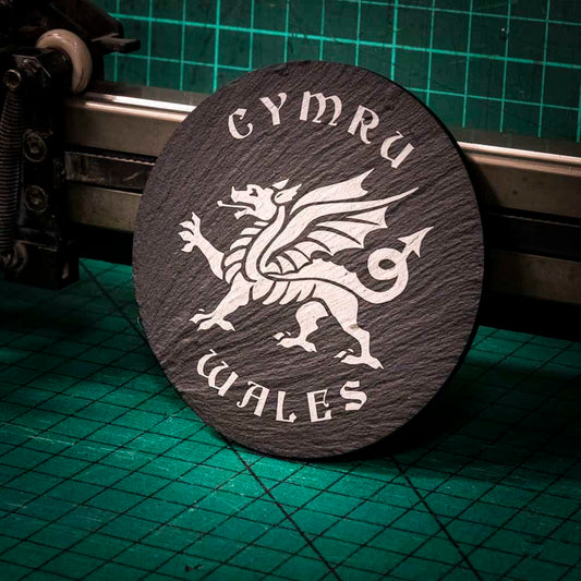 A laser engraved Welsh slate coaster with a welsh dragon in the center and the words cymru and wales