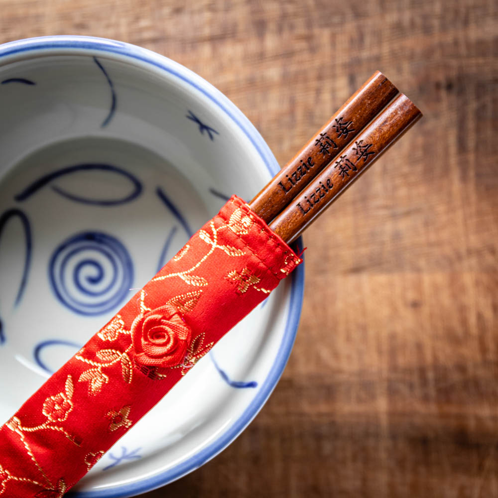 A pair of Japanese-style Chopsticks in a silk pouch, colour dark wood. The chopsticks are laser engraved and personalised with either a name or a phrase in English and are translated into either Chinese or Japanese.
