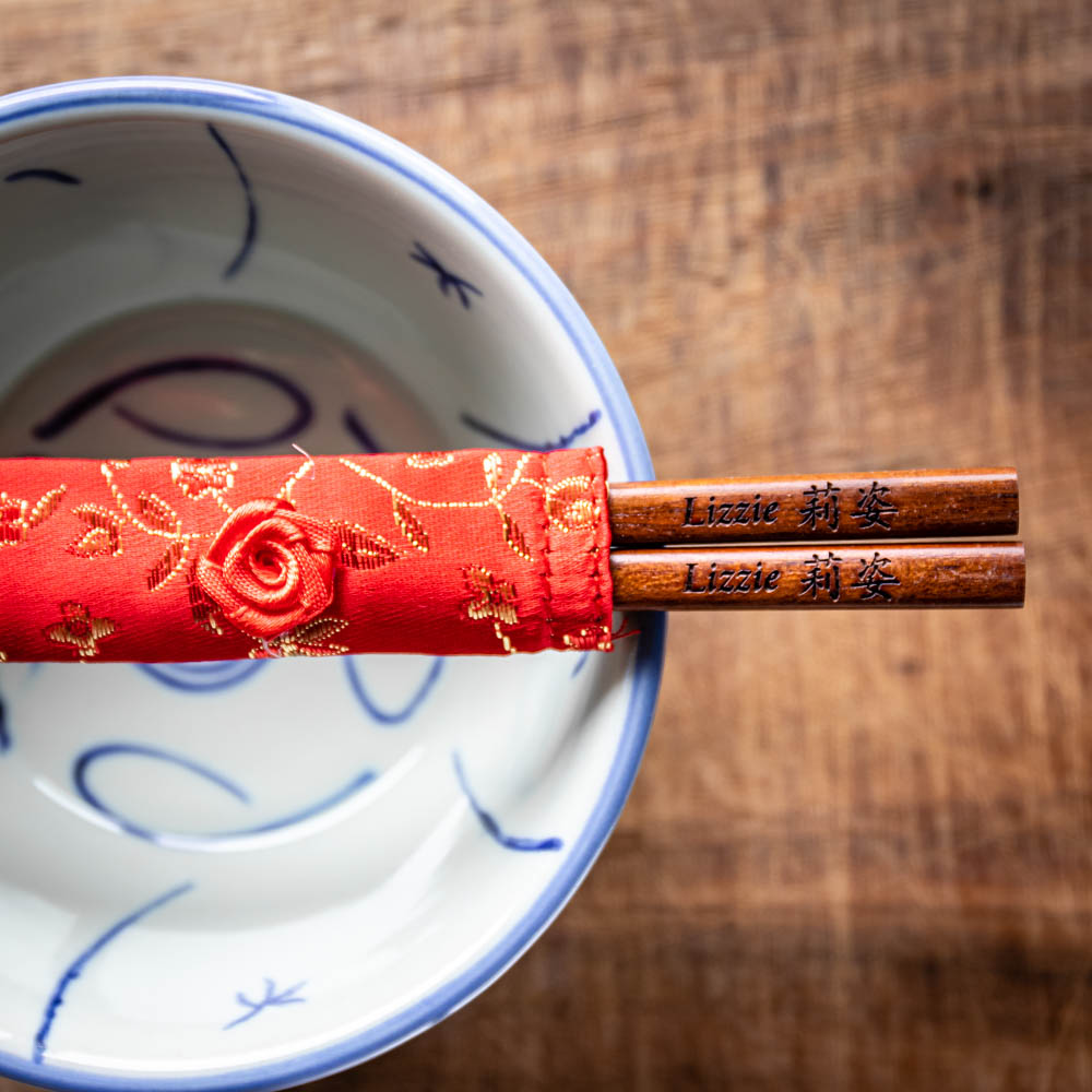 A pair of personalised dark wood Chinese Chopsticks, personalised with a name translated into Chinese in a Red silk chopstick pouch